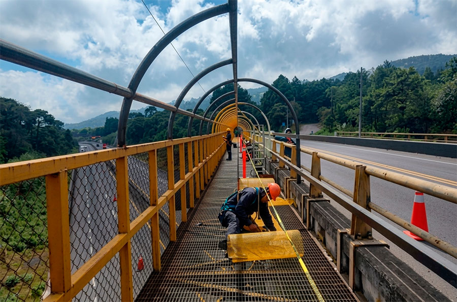 Trabajador dando mantenimiento a la estructura de un puente peatonal enjaulado sobre carretera